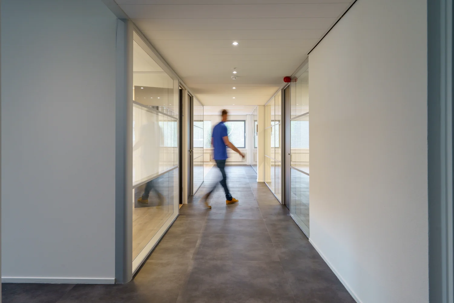 Man loopt door een moderne gang met glazen kantoordeuren aan de Baarnsche Dijk.